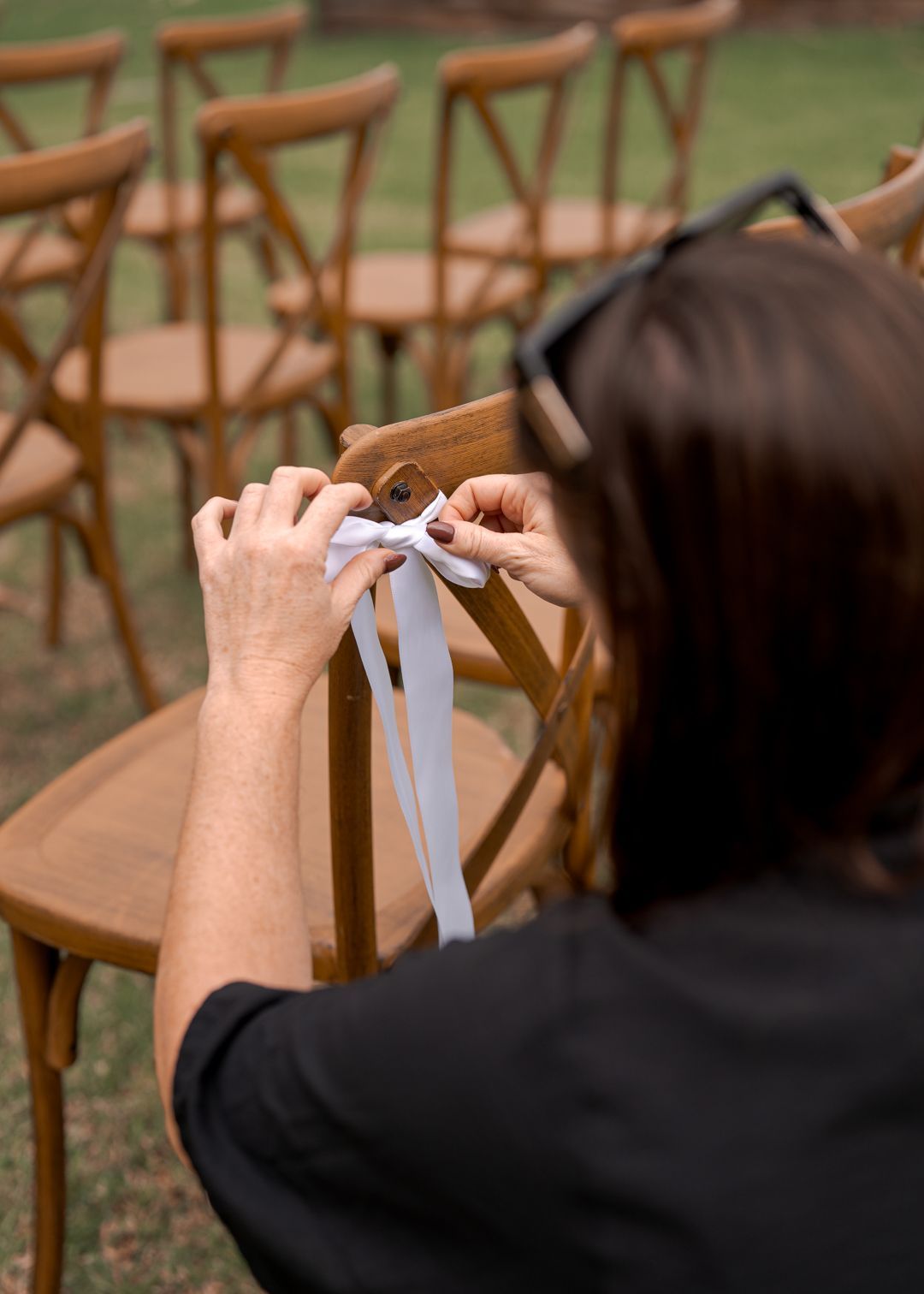 Person tying white ribbons onto an outdoor wooden chair