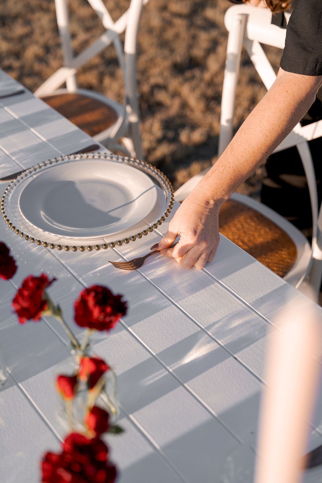 Hand setting a white plate on a sunlit outdoor table with a tablecloth