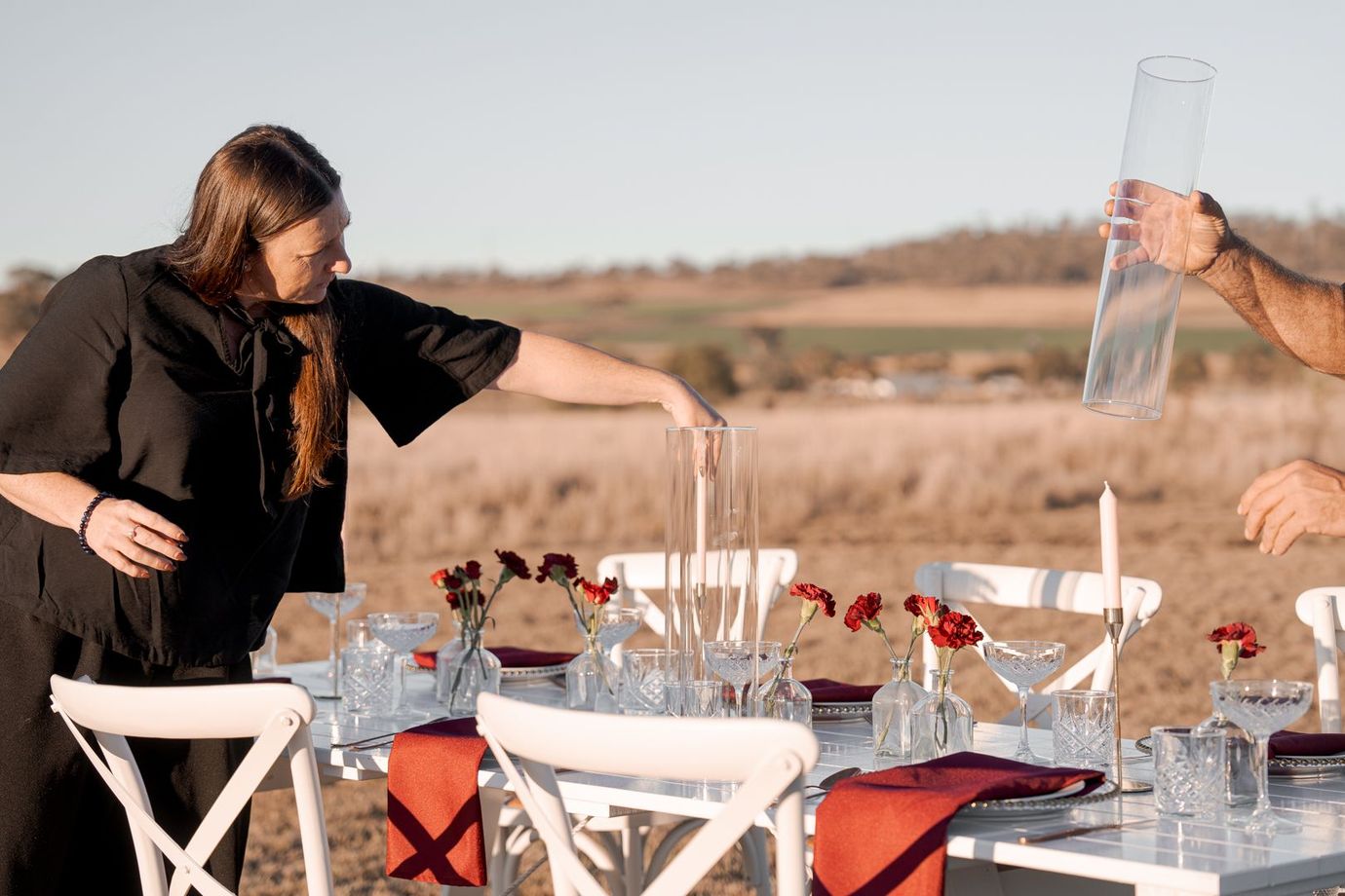 Woman arranging a table outdoors with drinks and chairs in a sunny field