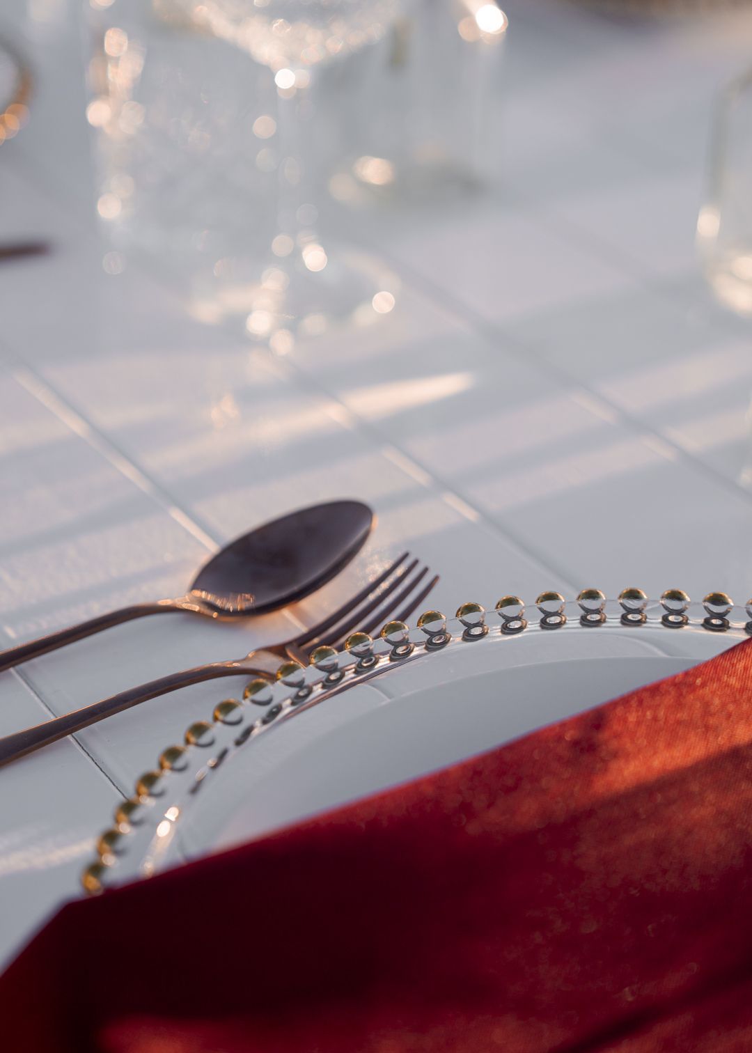 Elegant table setting with silverware, beaded charger, and red napkin.