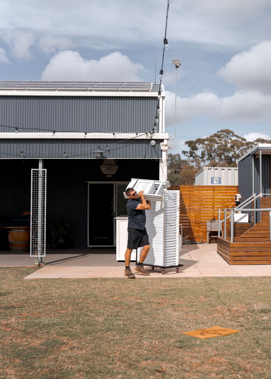 Person carrying a stack of white chairs outside a metal building.
