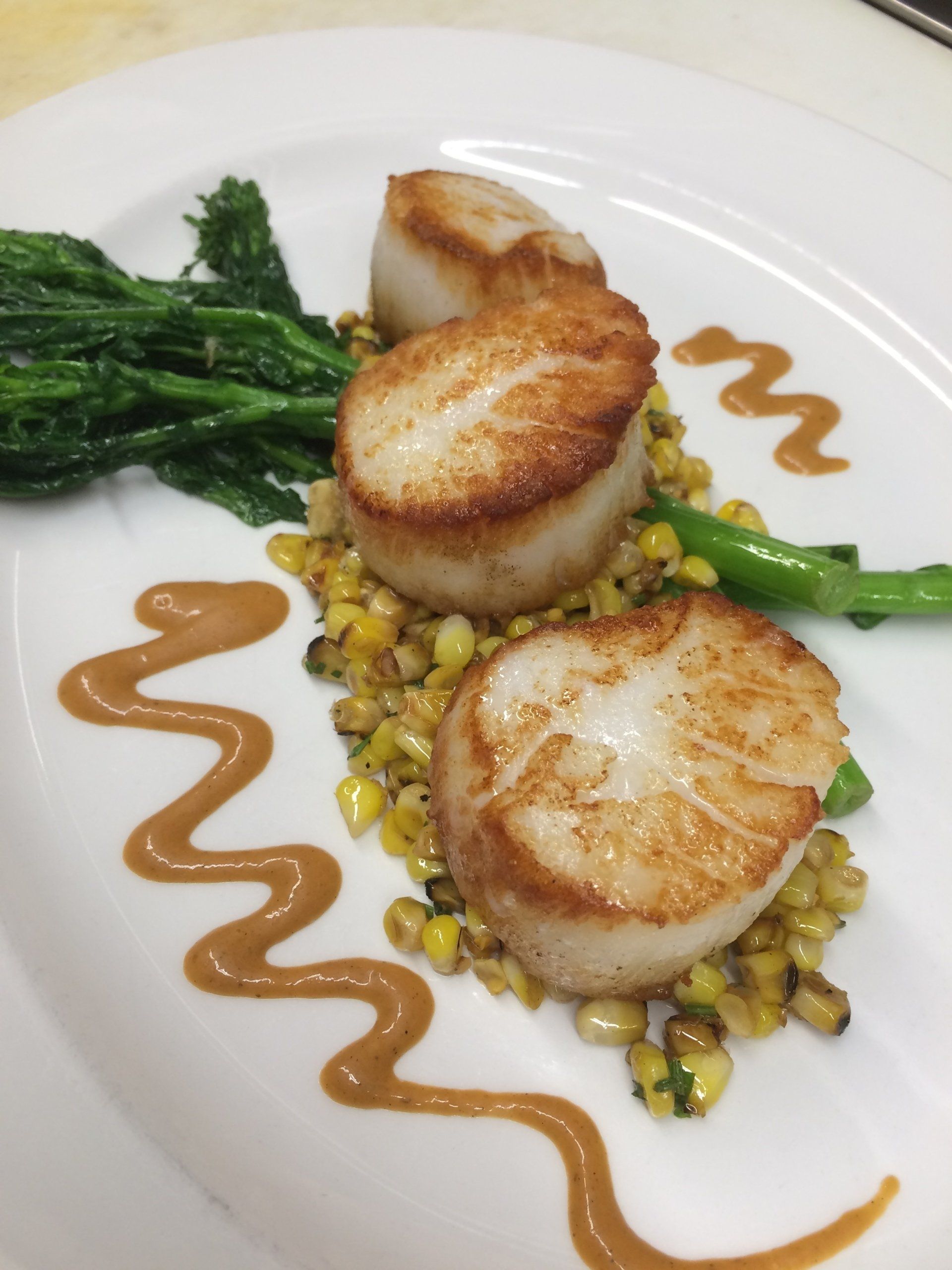 A white plate topped with scallops corn and greens