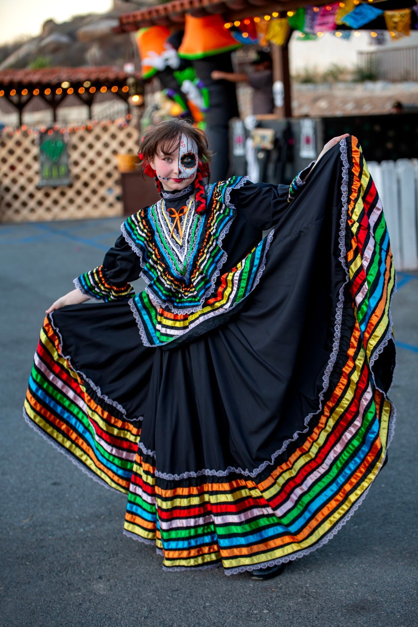 Person in a black dress with rainbow trim dancing in a street festival setting