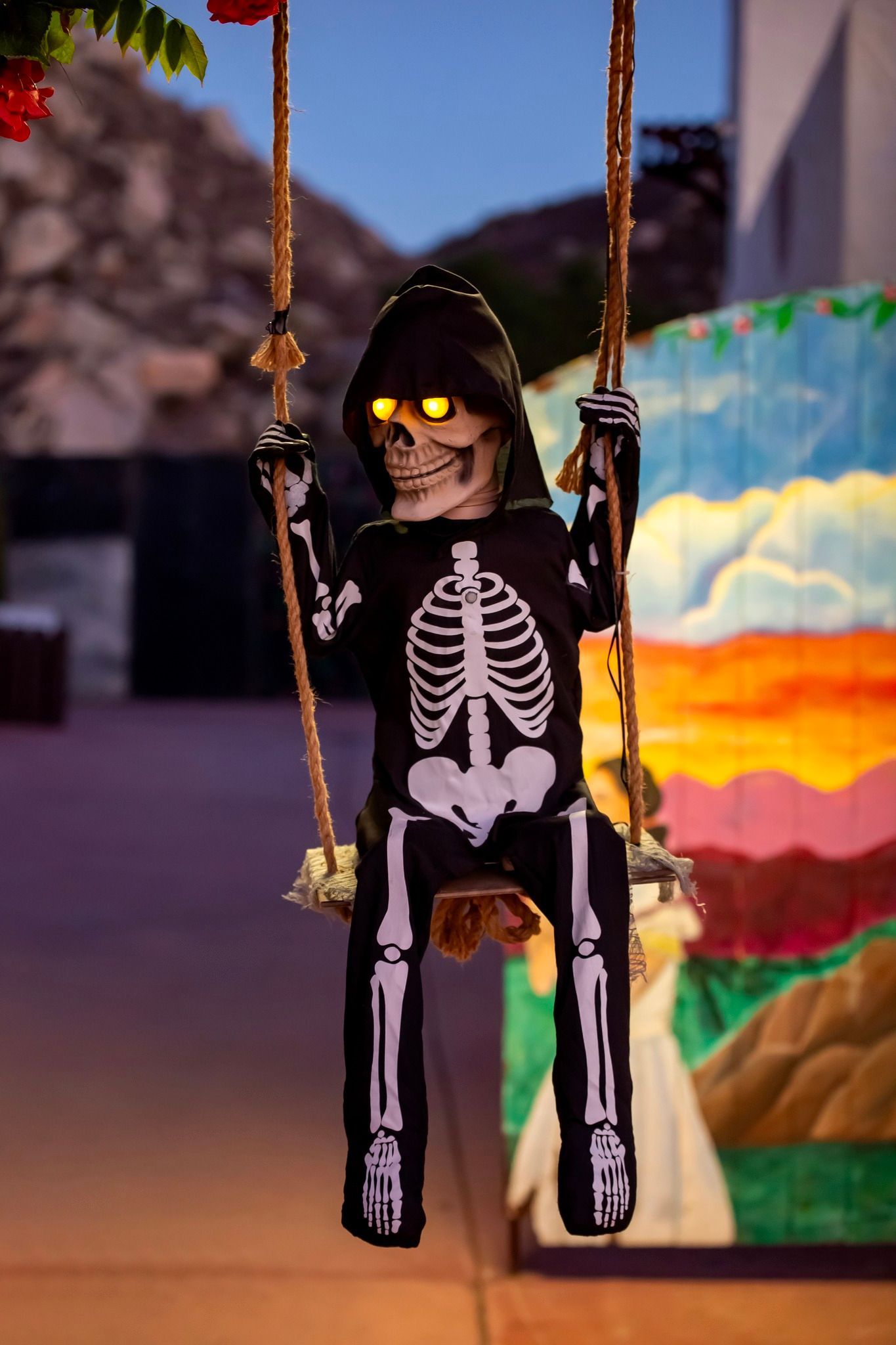 Skeleton Halloween decoration hanging from ropes, with glowing eyes, in front of a colorful mural
