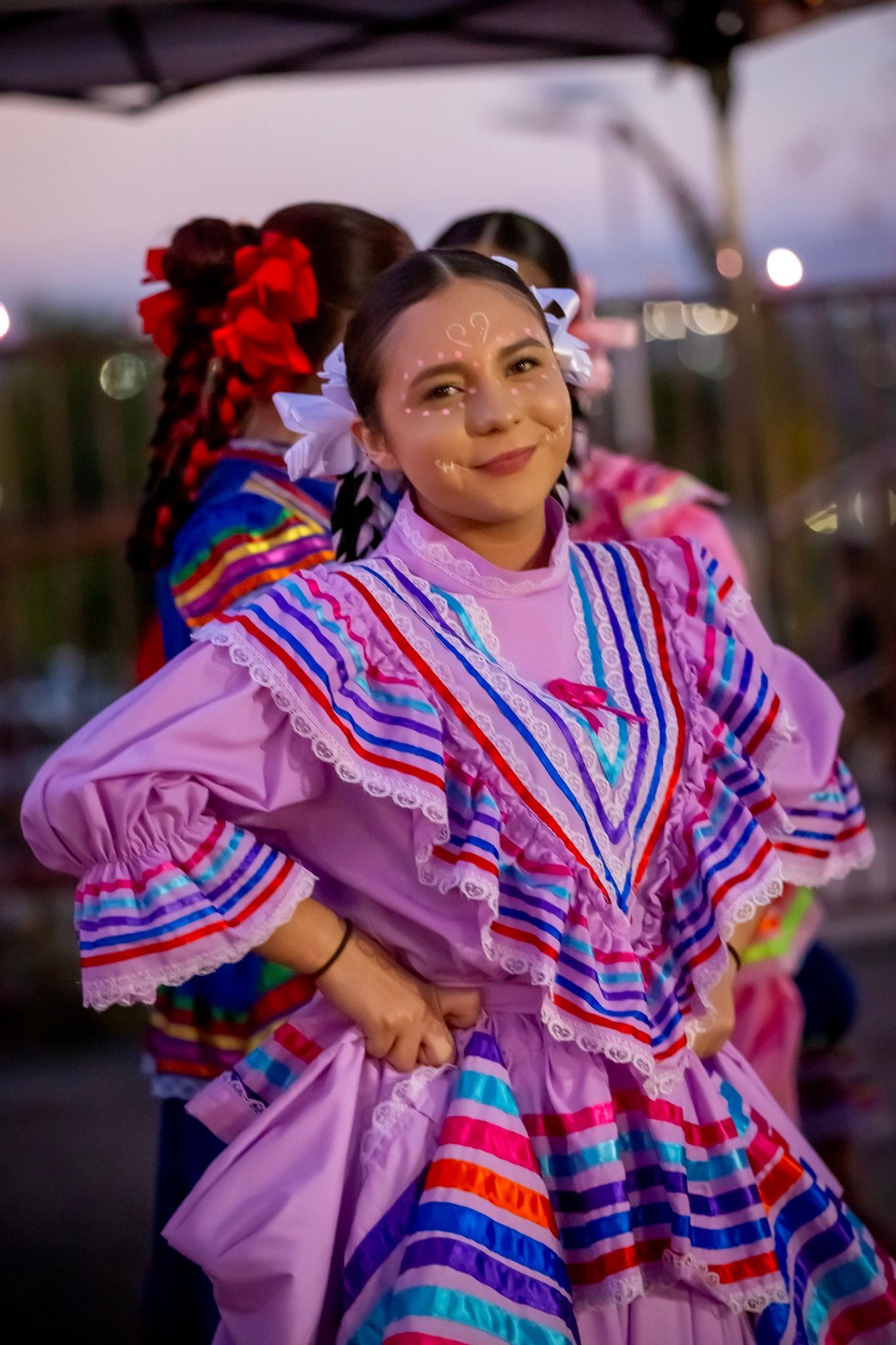 Woman in a colorful embroidered dress smiling at an outdoor cultural event