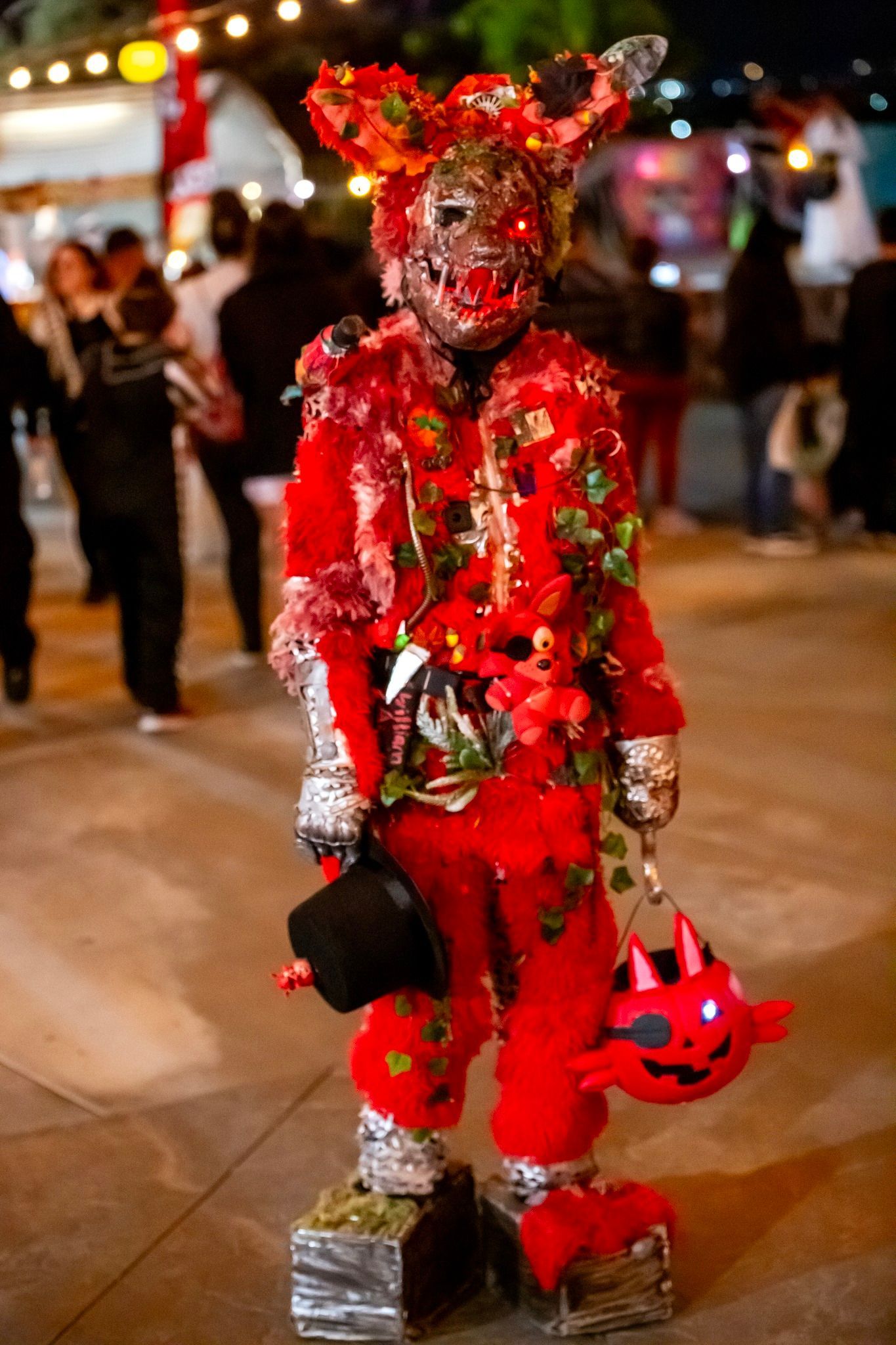 Red costumed figure with horns and a red mask standing at a nighttime street festival