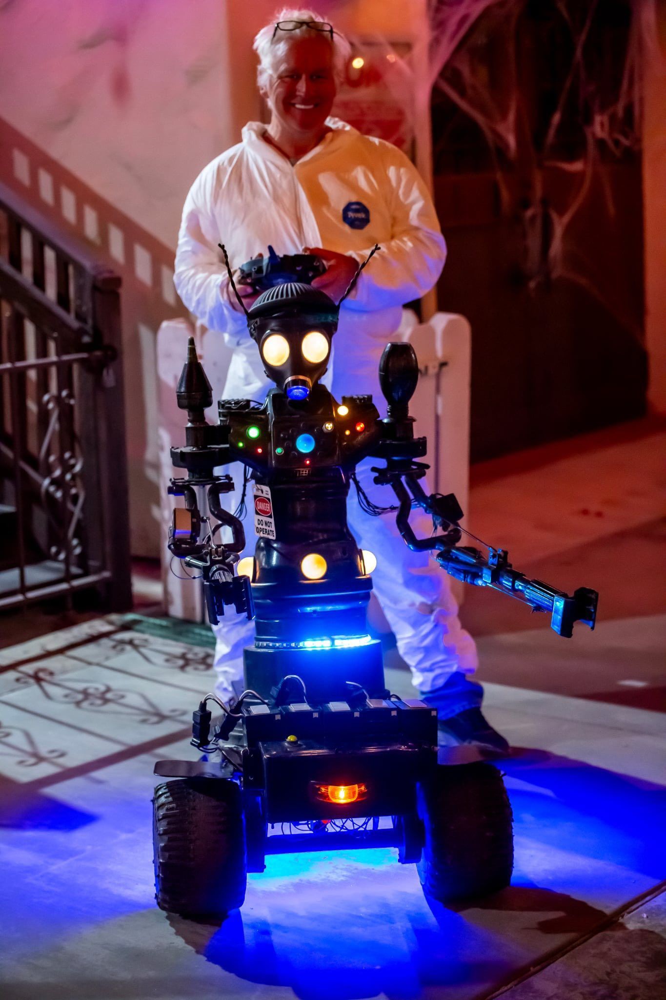 Person standing on a lit robot at night, with blue and orange lights in a hallway