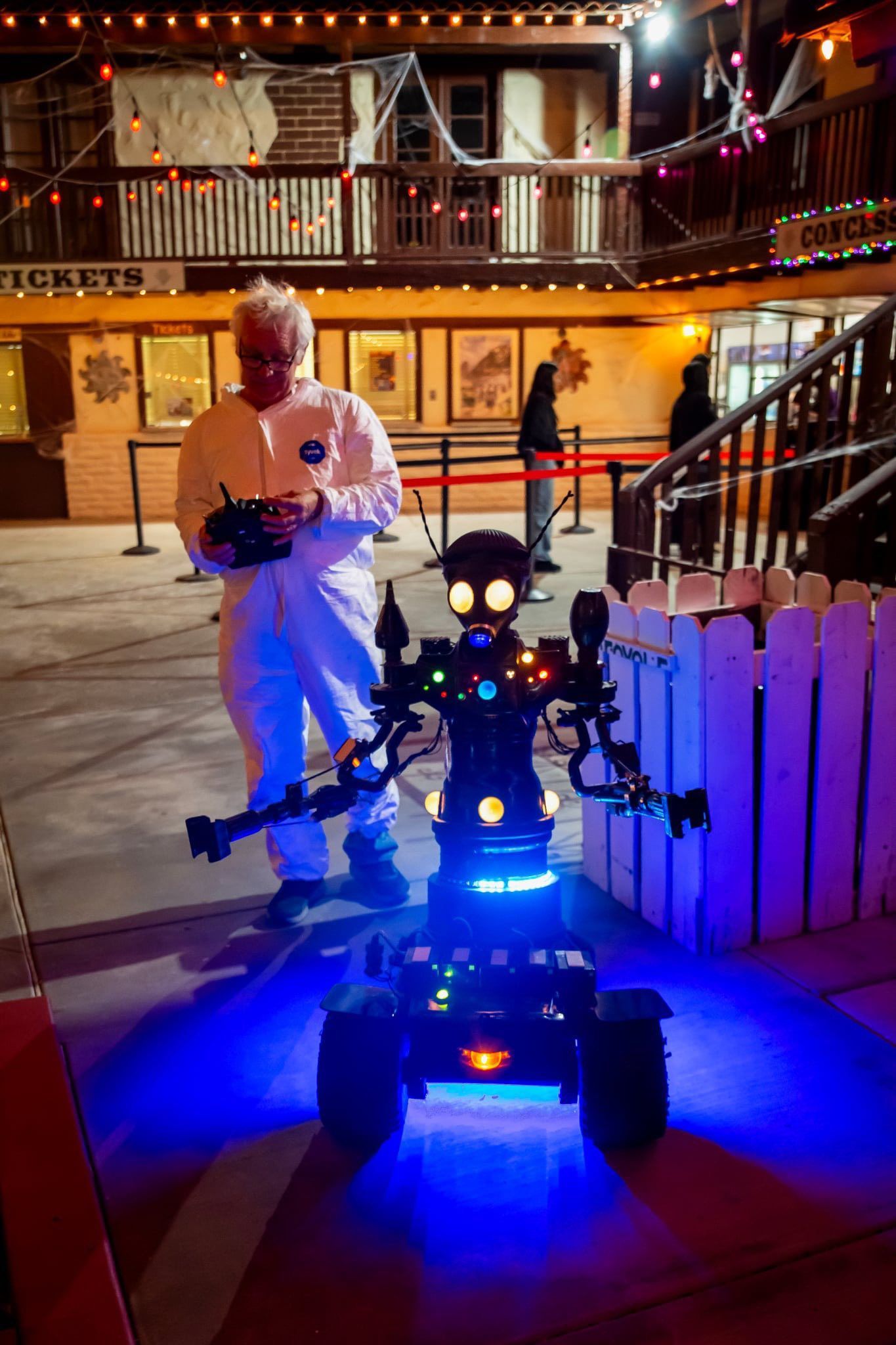 Person standing beside a lit robot in a decorated outdoor courtyard at night