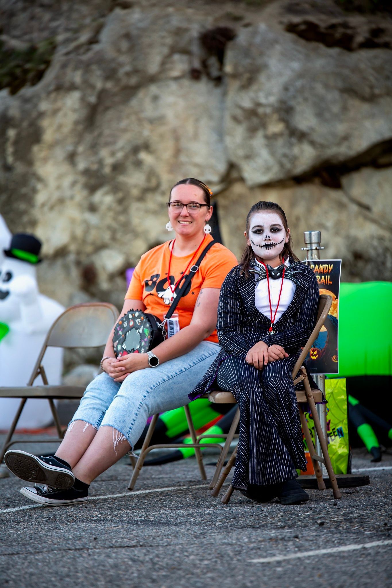 Two seated performers in Halloween makeup, one in orange shirt and one in black costume, against a rocky backdrop