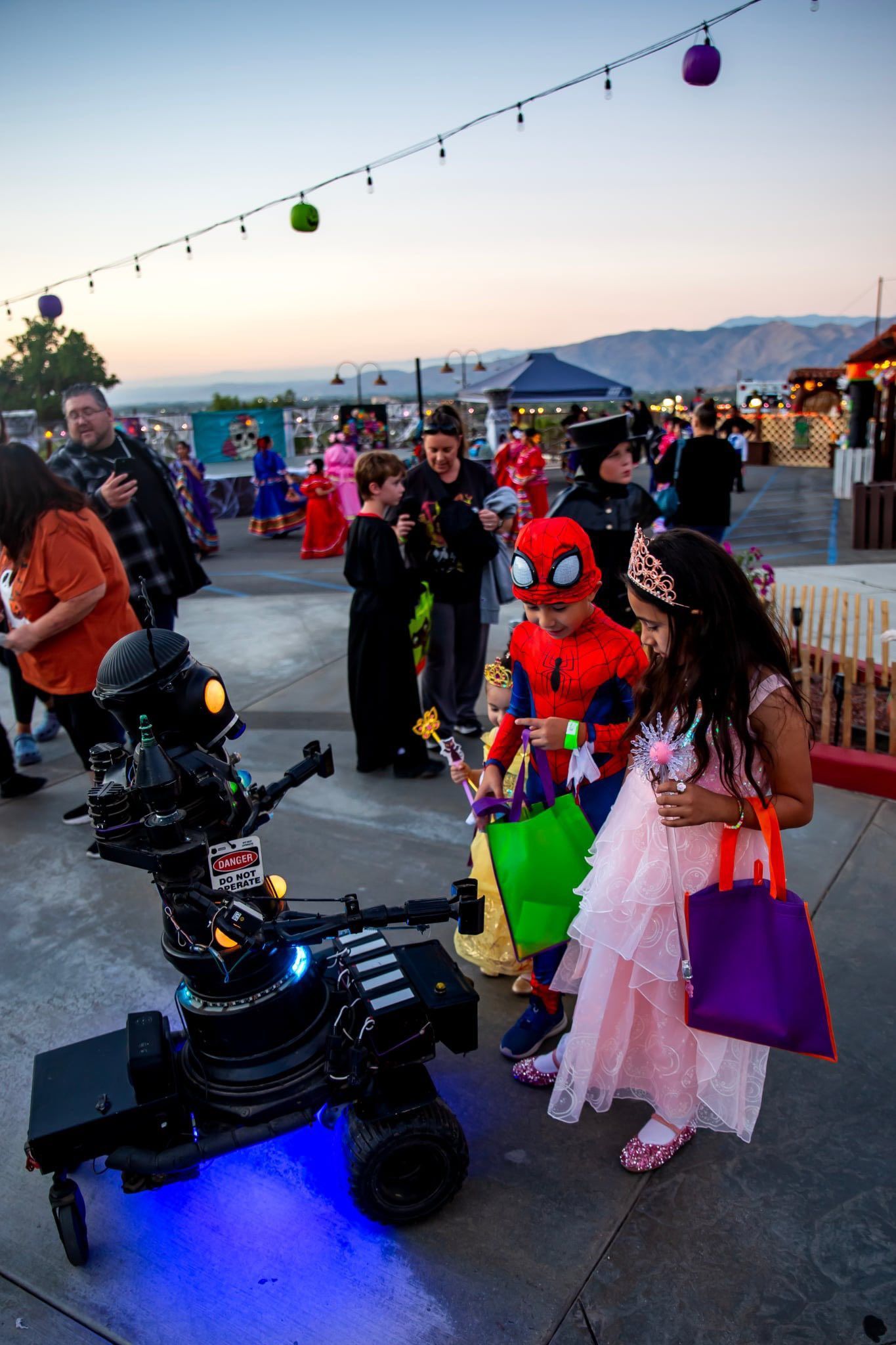 Spiderman-costumed child with neon-lit robot at a lively outdoor evening event