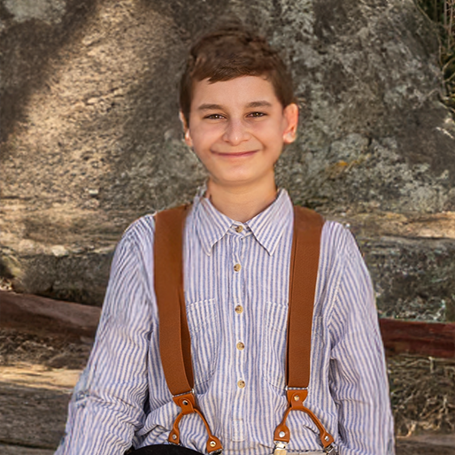 Smiling child in a striped shirt with suspenders standing in front of a rocky backdrop
