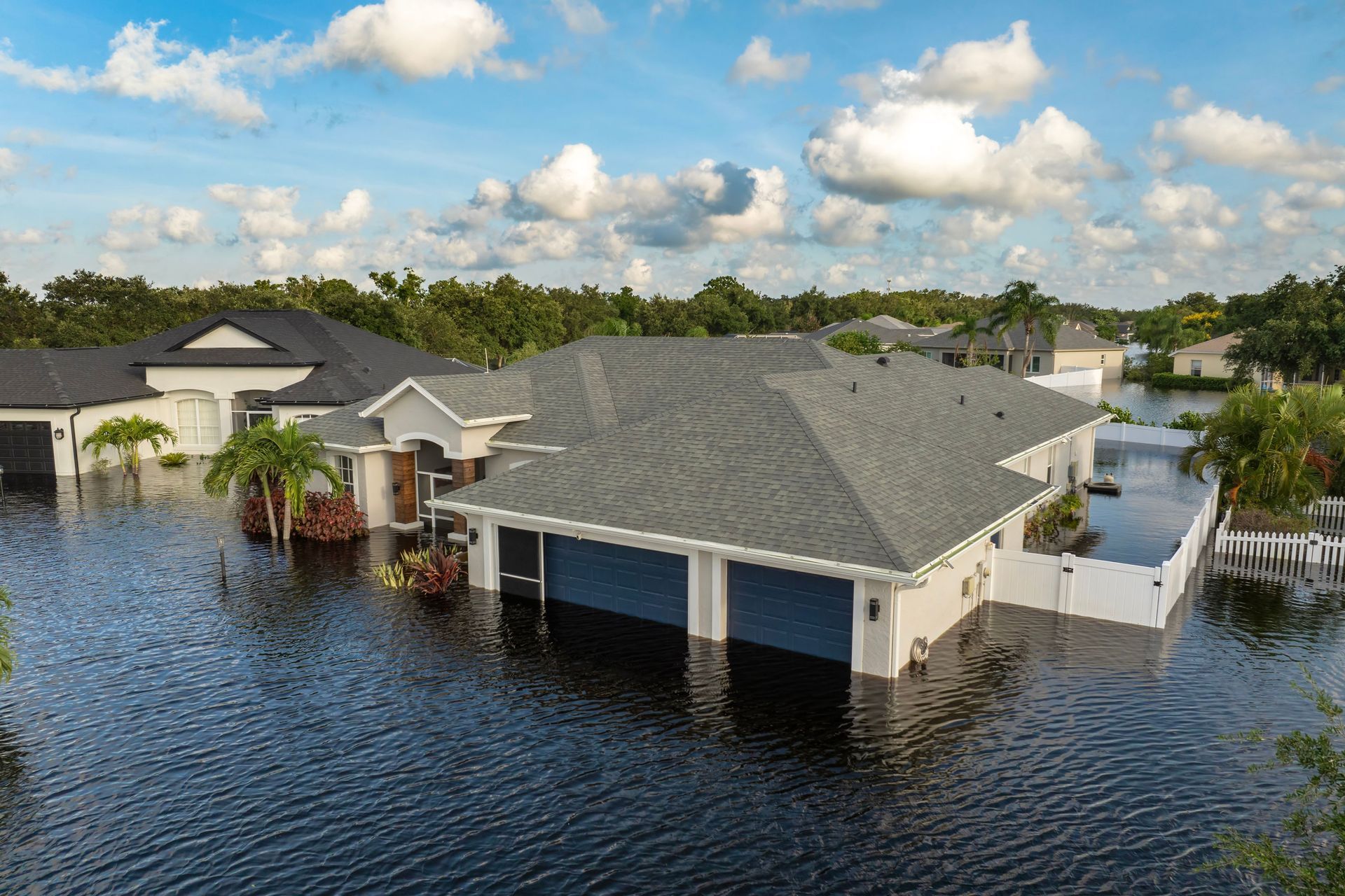 Flooded houses in a neighborhood after a hurricane, with floodwaters up to the garage doors.