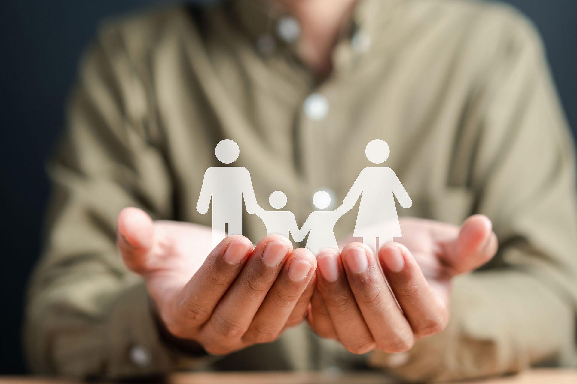 Person cupped hands holding a paper cutout of a family, symbolizing care and protection.