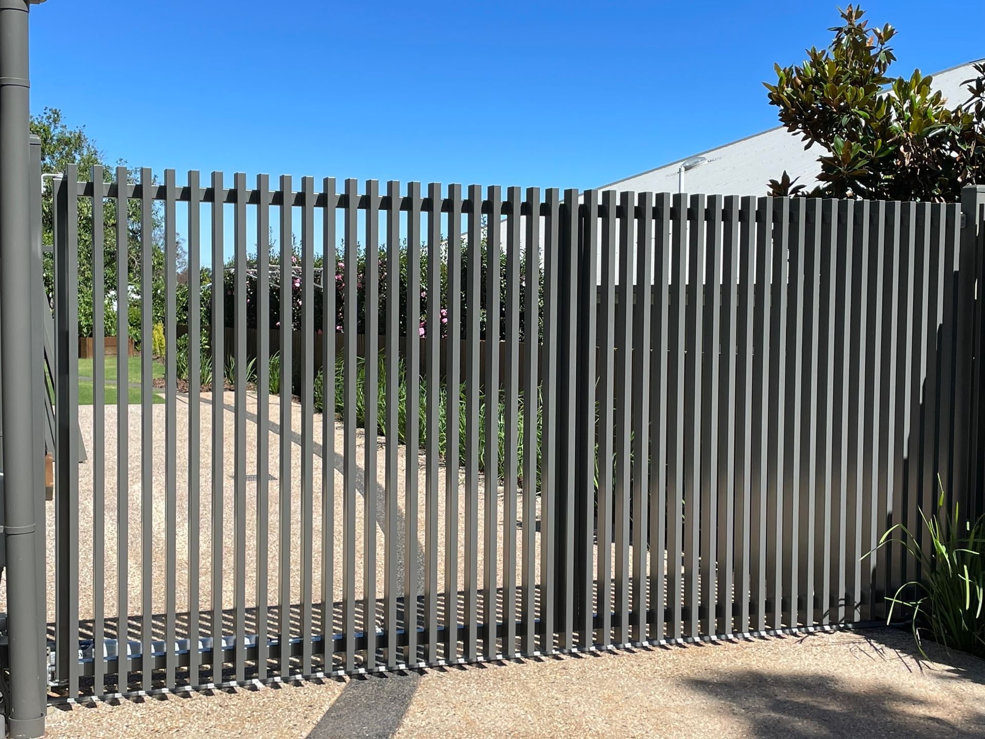 A large metal fence is surrounding a gravel driveway.