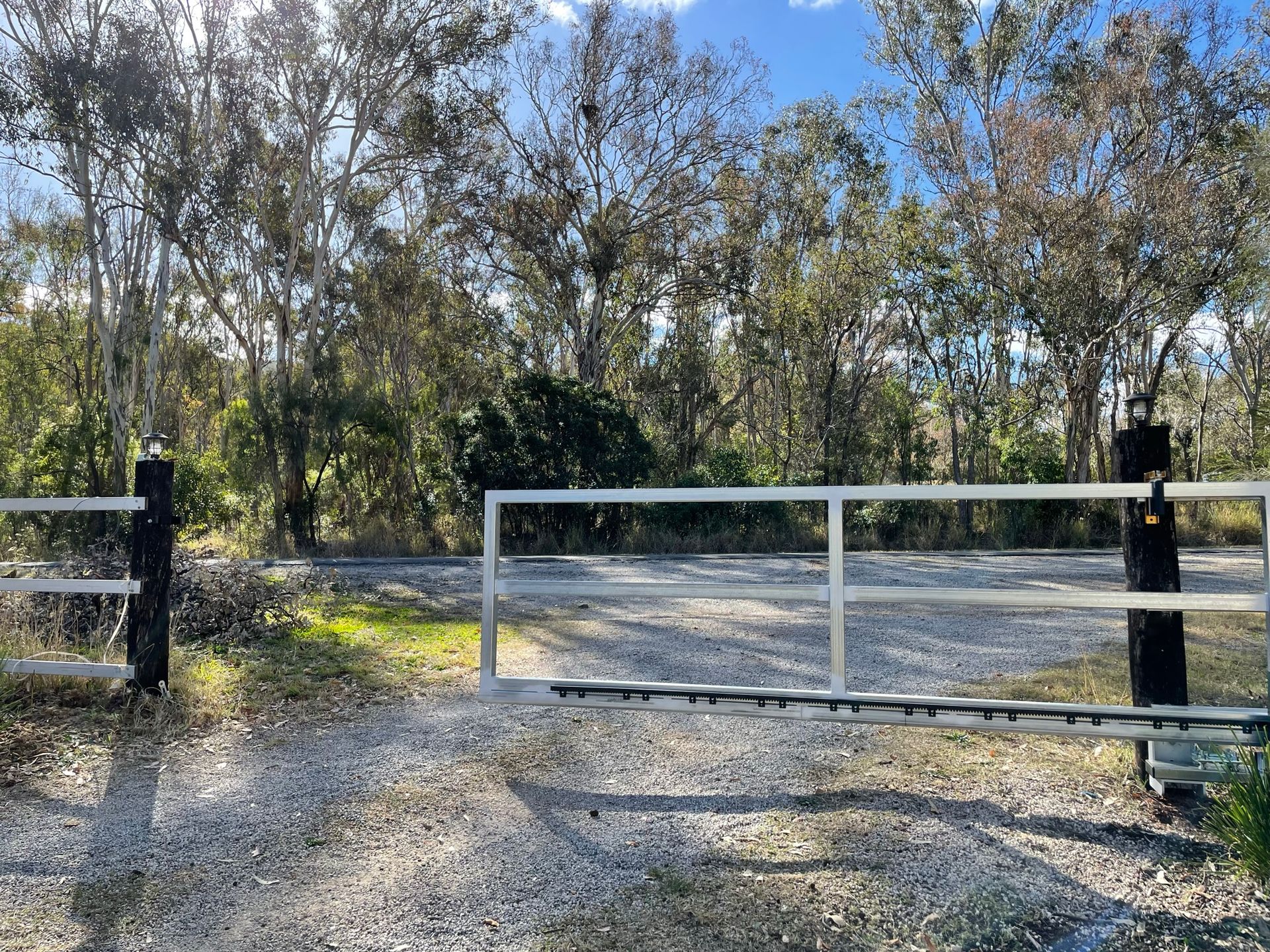 A white gate is sitting in the middle of a gravel road.