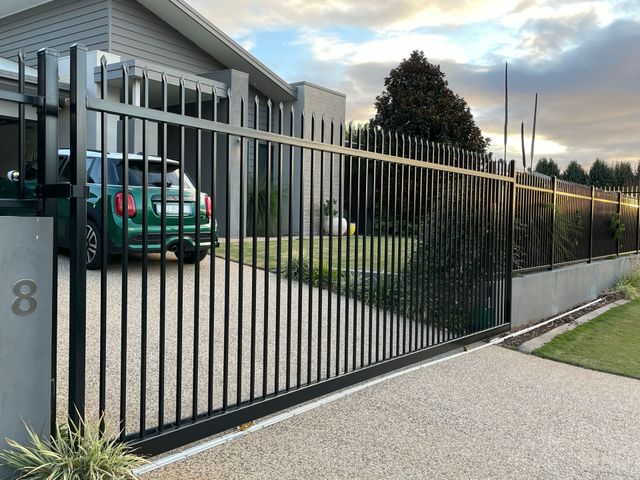 A green car is parked in front of a sliding gate.