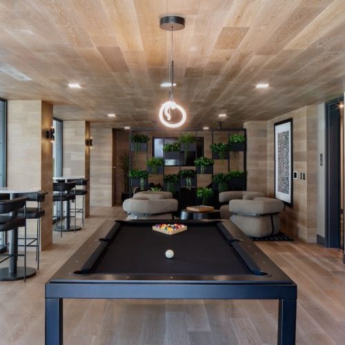 Indoor community lounge with a billiards table, surrounding seating, and indoor plants at Sofia, offers pet-friendly apartments in Santa Clara.