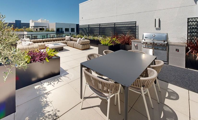 Rooftop outdoor terrace with a dining table, chairs, lounge seating, planters, and a grill at Sofia, offers pet-friendly apartments in Santa Clara.