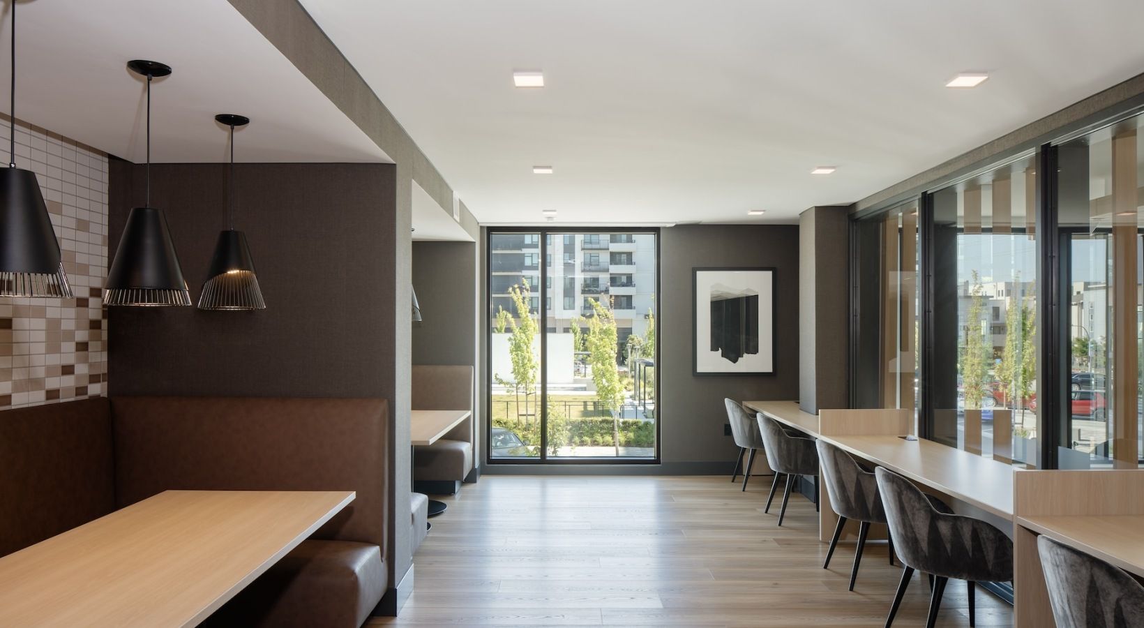 Modern apartment community lounge with booth seating and a long desk by large windows at Sofia, offers Santa Clara apartments for rent in CA.