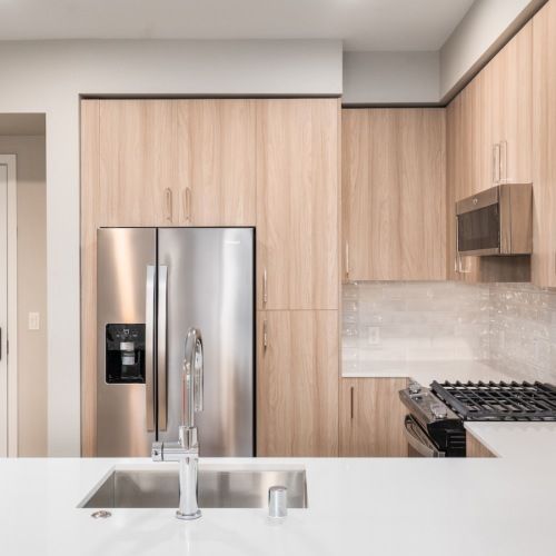 Modern apartment kitchen with stainless steel fridge, light wood cabinets, and a white island at Sofia, offers pet-friendly apartments in Santa Clara.