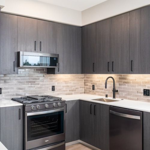 Modern apartment kitchen with dark wood cabinets, stainless steel appliances, and a white countertop at Sofia, offers pet-friendly apartments in Santa Clara.