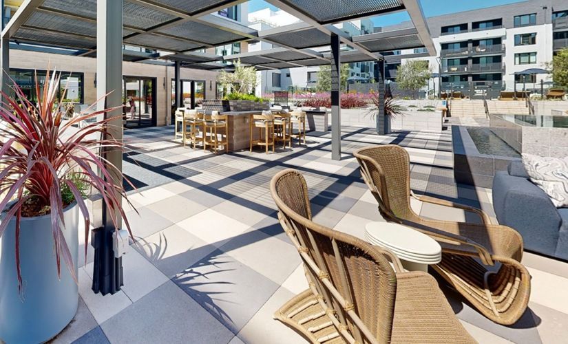 Outdoor communal patio with wicker lounge chairs, high-top tables under a pergola, near a pool at Sofia, offers pet-friendly apartments in Santa Clara.