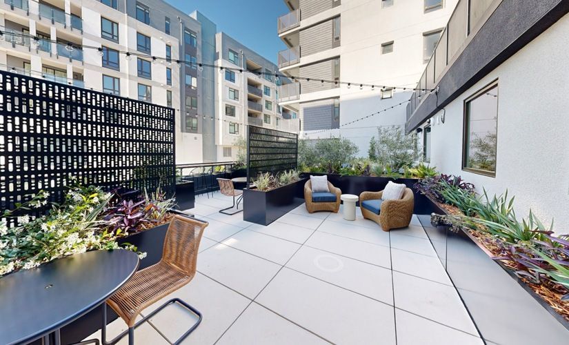Outdoor communal terrace with seating, planters, and string lights in a modern apartment complex at Sofia, offers pet-friendly apartments in Santa Clara.