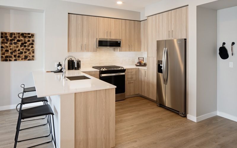 Modern apartment kitchen with an island, stainless steel fridge and stove, and light wood cabinets at Sofia, offers pet-friendly apartments in Santa Clara.
