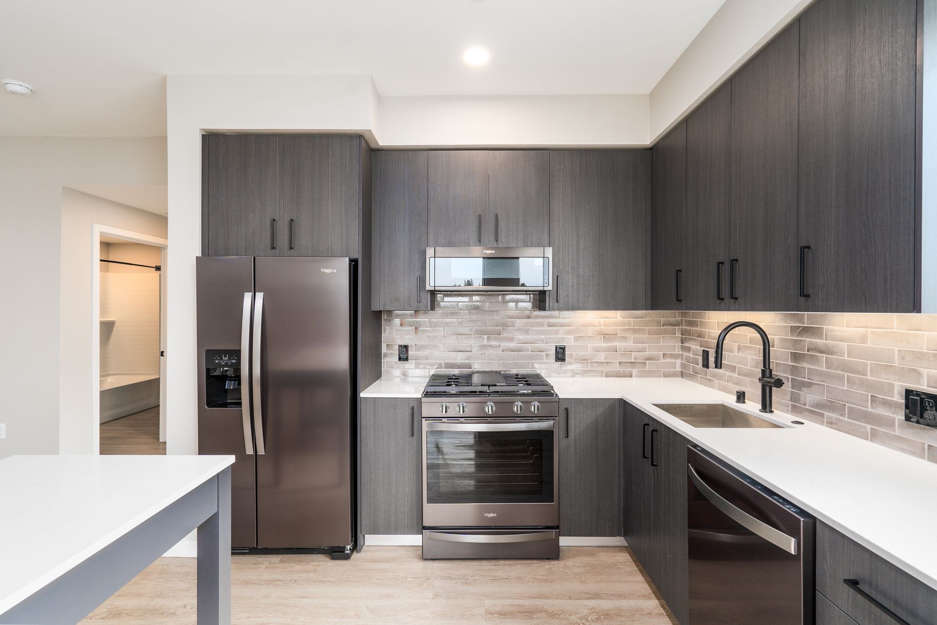 Modern kitchen with dark gray cabinets, stainless steel appliances, and white countertops.