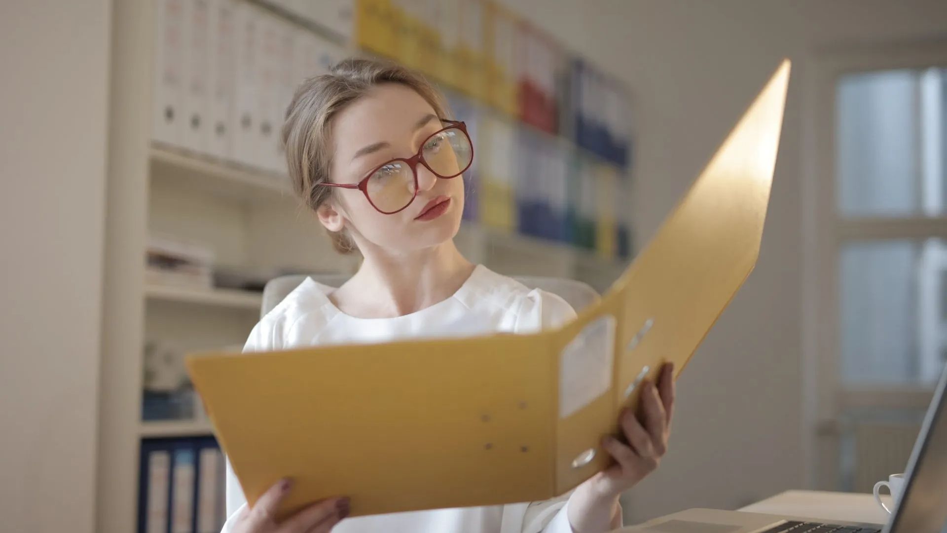 a woman is sitting at a desk holding a folder and looking at it .