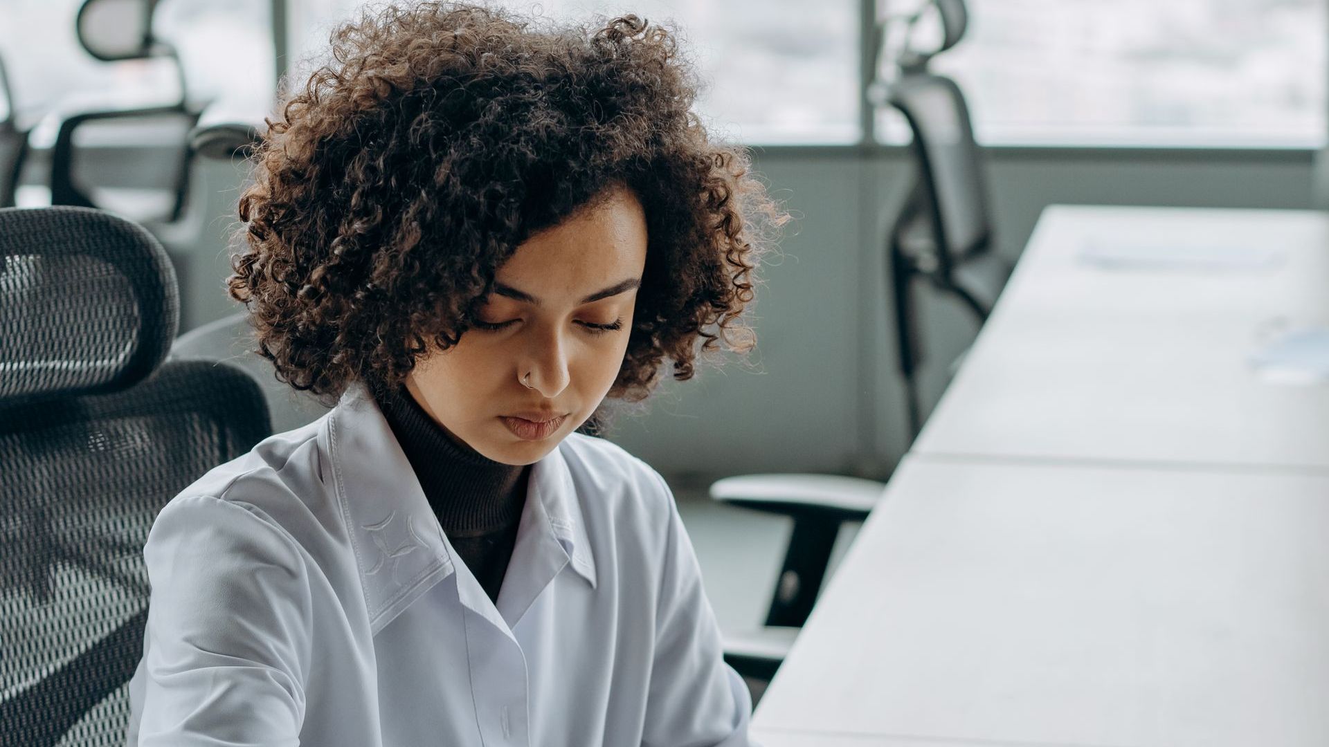 a woman in a lab coat is sitting at a desk in an office .
