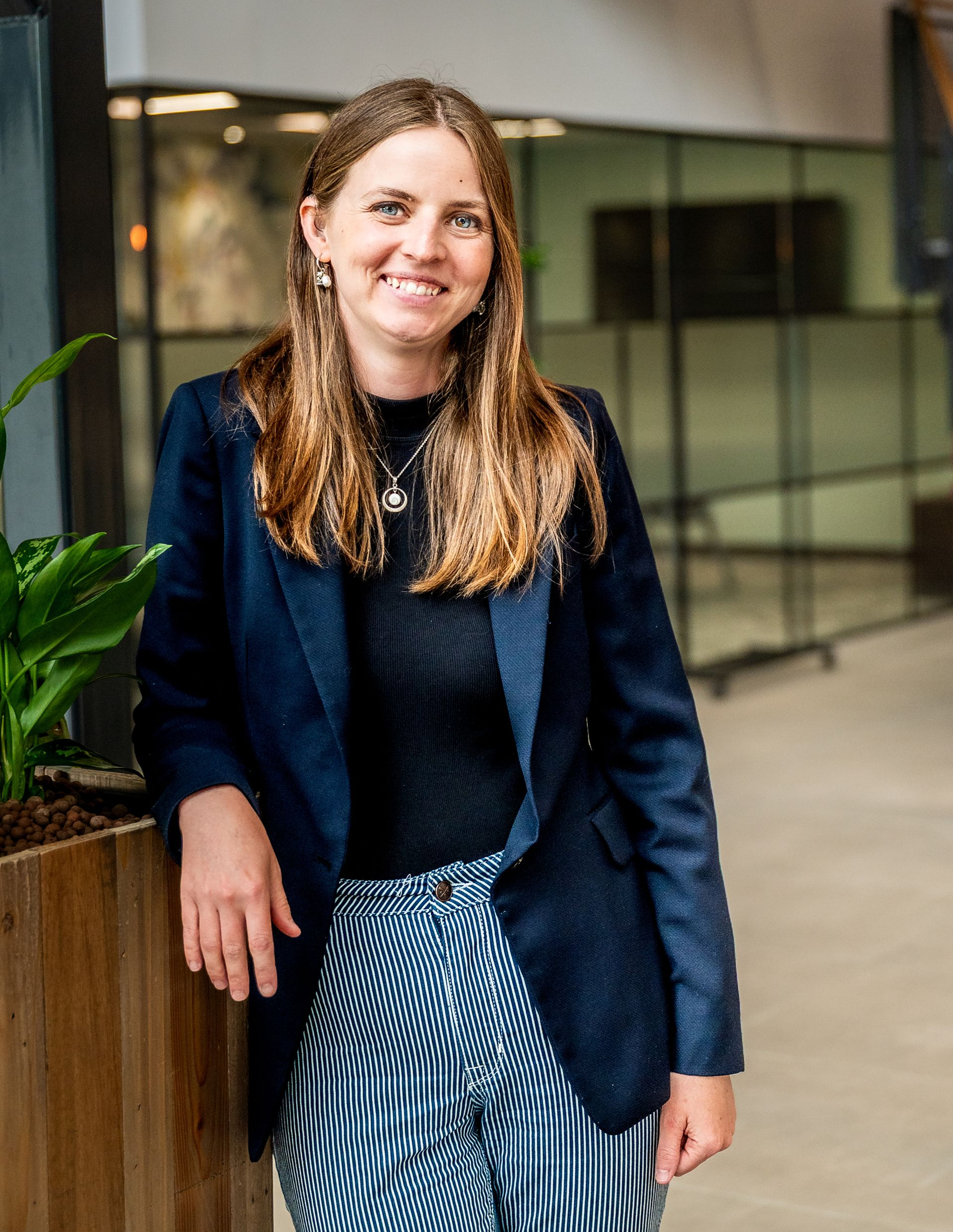 Woman standing in a modern office in a blue blazer and patterned skirt.