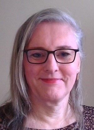 A woman wearing glasses and earrings is smiling for the camera.