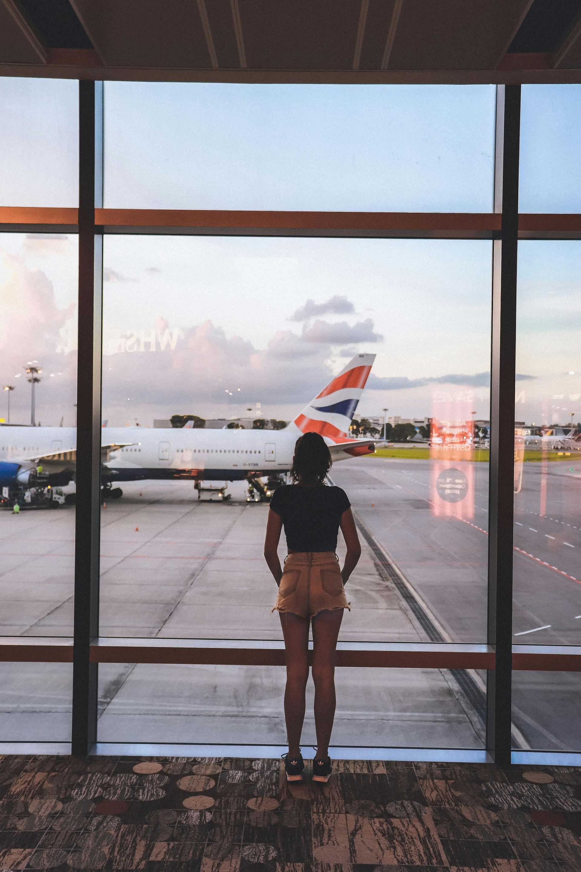 A woman is looking out of an airport terminal building window at an aeroplane on the apron.