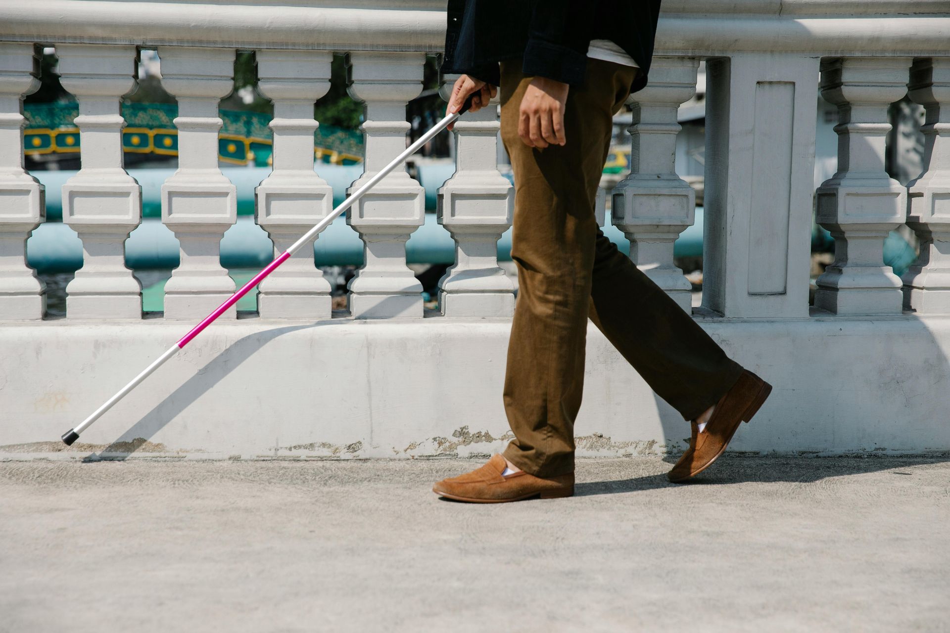 A blind man is walking across a bridge with a cane.
