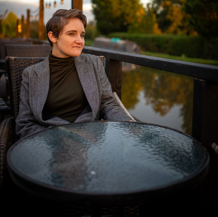 Nina Condron seated at an outdoor table beside a reflective waterway at sunset