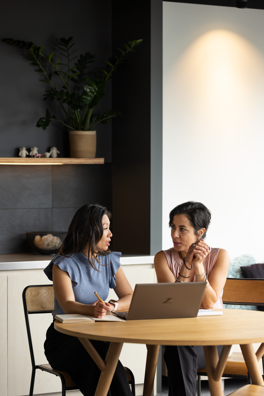 Two people talking at a wooden table with a laptop in a modern, softly lit room