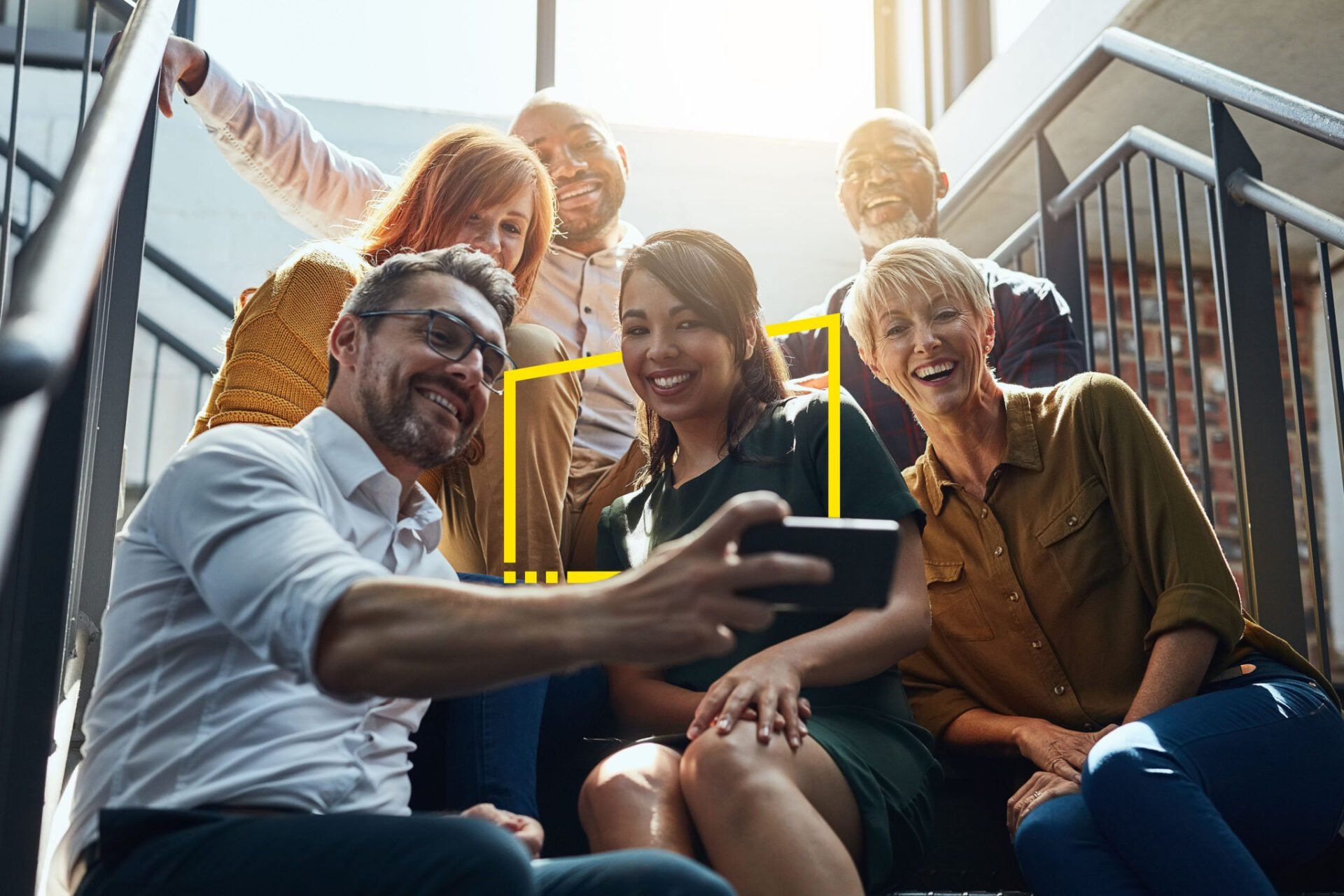 colegas de trabalho tiram foto sorrindo em uma escada. entre os colegas estão maturis e colaboradores mais jovens.