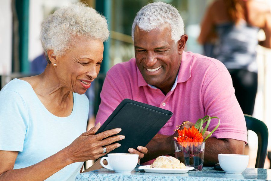 dois mauturis estão sentados tomando café, ambos sorriem satisfeitos olhando para a tela de um tablet. o homem veste rosa e a mulher azul.