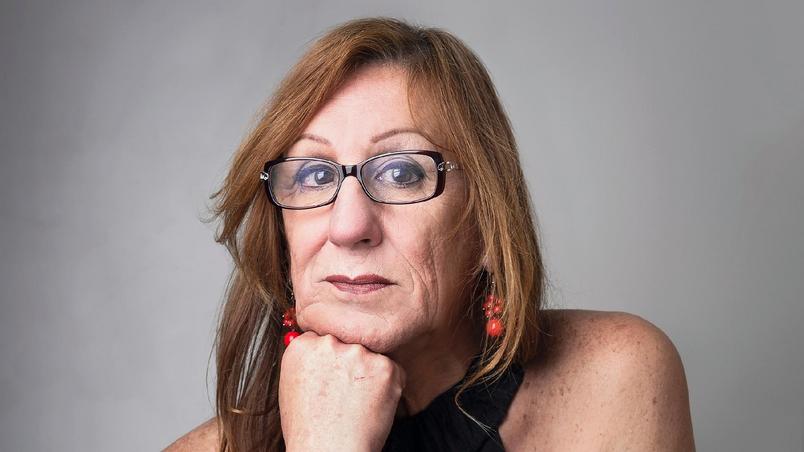 mulher posa para a foto com o rosto apoiado na mão. ela usa óculos de grau com armação preta