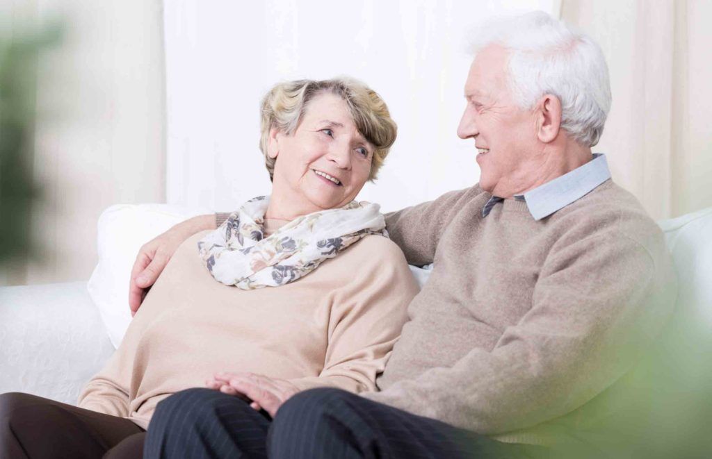 casal de maturis felizes olhando e sorrindo um para o outro, ambos vestem suéteres de cor bege