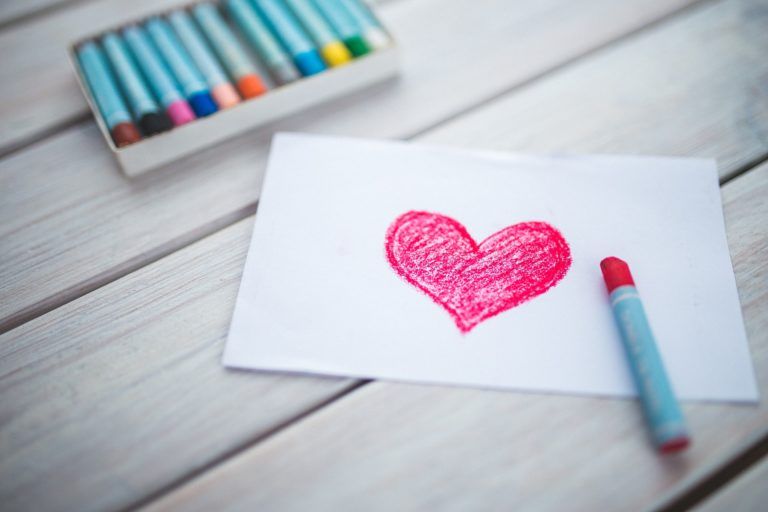 papel branco com coração rosa desenhado. ao lado estão canetinhas coloridas.