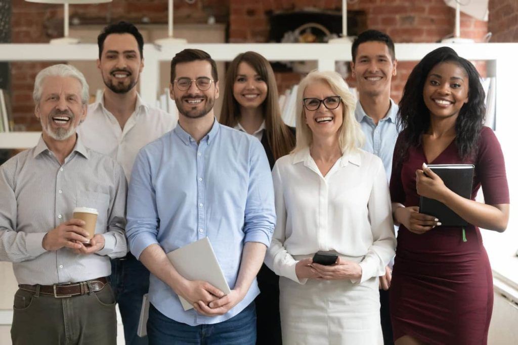 maturis posando com colegas de trabalho mais novos. todos sorriem e aparentam felicidade