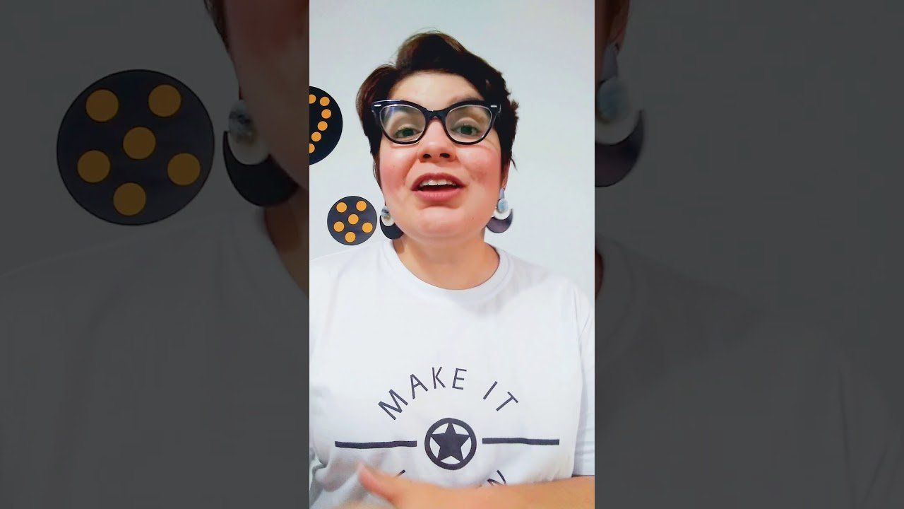 mulher fala em frente a câmera. ela tem os cabelos curtos, usa camiseta branca escrito 