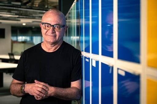 Paulo Ferrari, um dos maturis contratados pelo banco Neon. Ele posa de camiseta preta e mãos dadas, aparenta contentamento