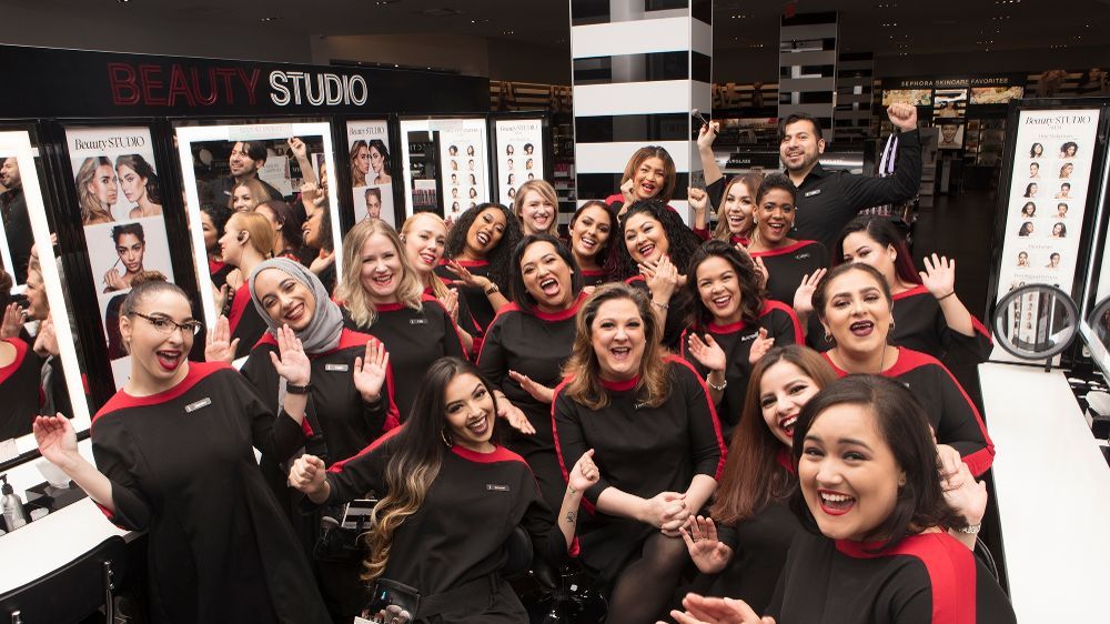 equipe da sephora. na foto há mulheres de diversas etnias, elas vestem um vestido preto com uma faixa vermelha nos ombros