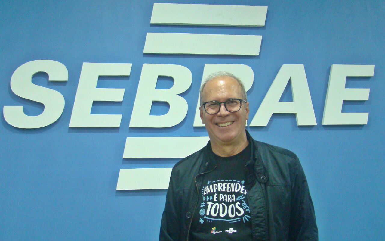 homem para em frente ao logo do Sebrae, ele sorri.