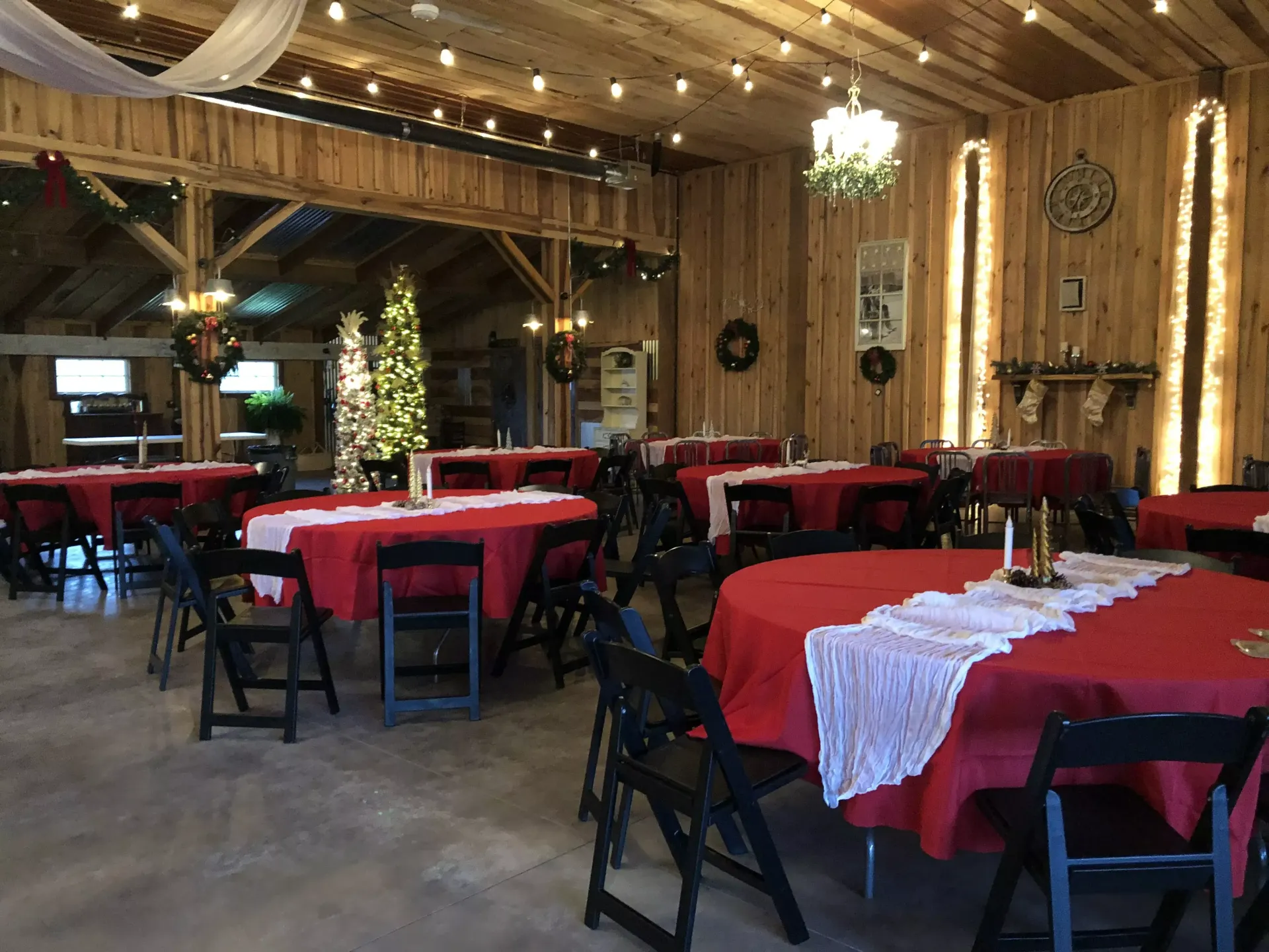 Rustic dining hall with red tablecloths, black chairs, wooden beams, and warm chandeliers