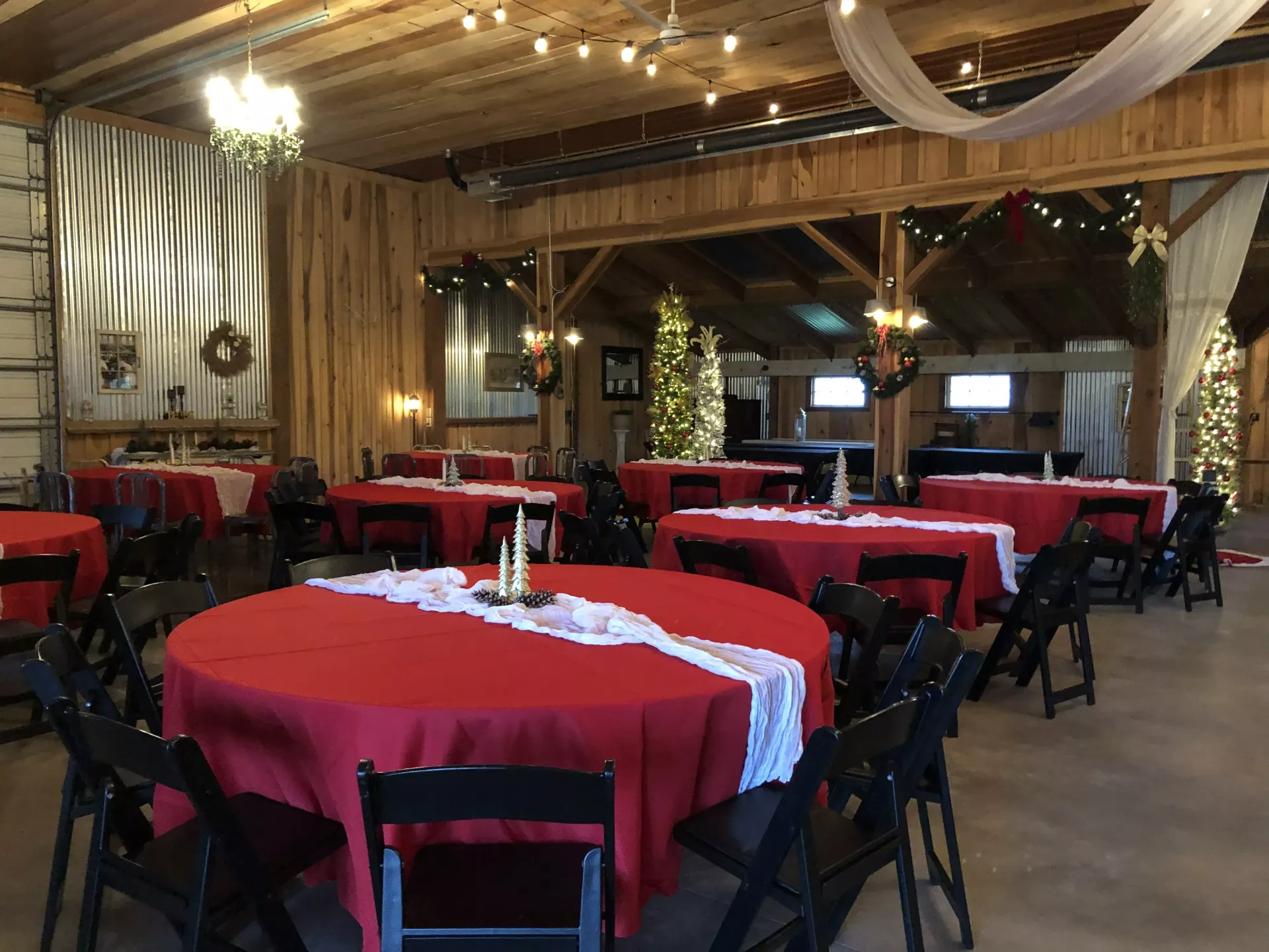 Rustic banquet hall with red tablecloths, black chairs, and wooden beams under warm string lights