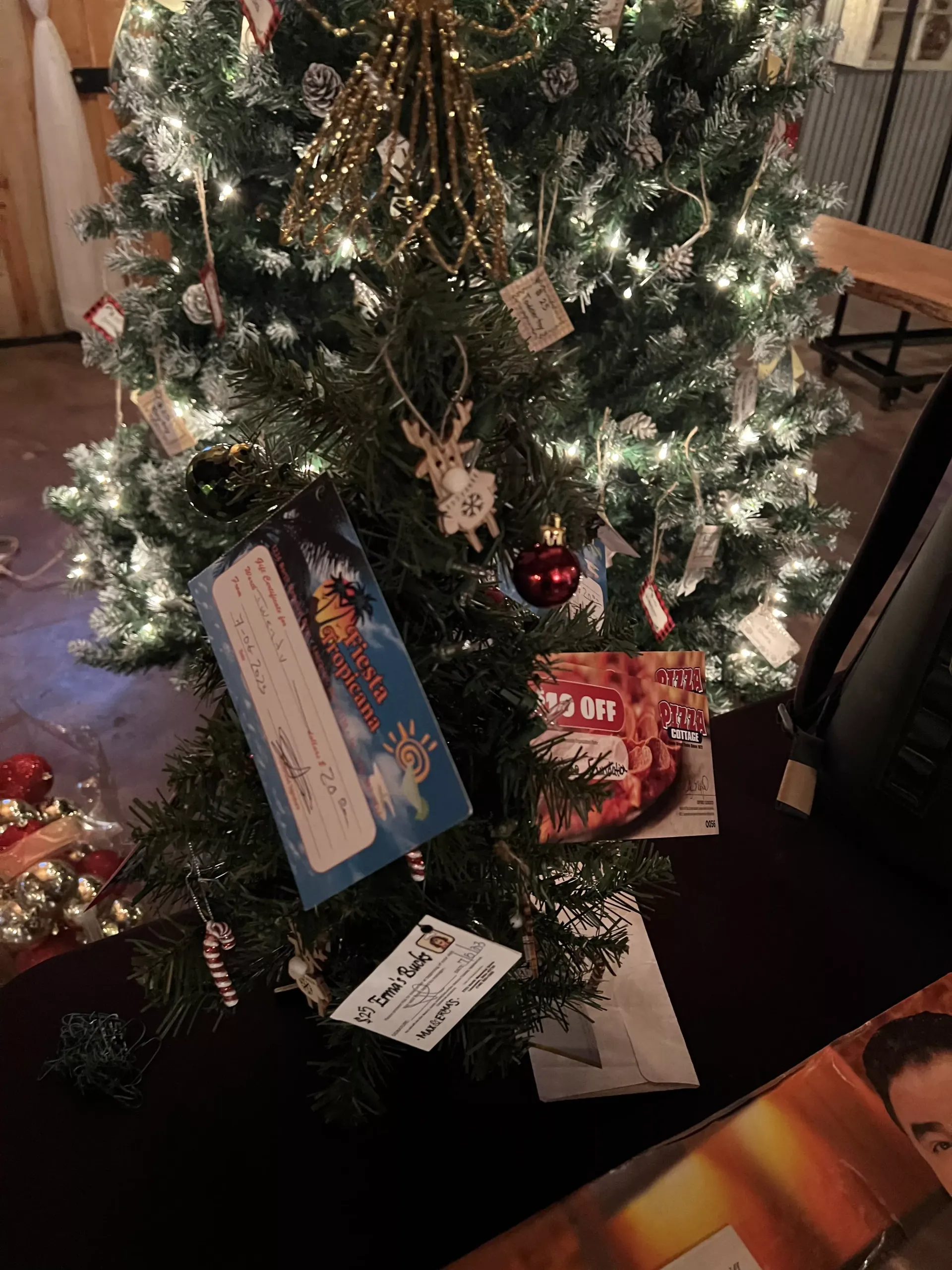 Christmas tree with wrapped gifts and ornaments at the base, indoors, lit with white lights